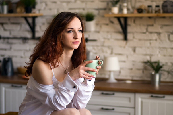 Adorable nice charming cheerful pretty trendy stylish girl drinking coffee, sitting on table countertop in modern light white kitchen - Foto, Imagen