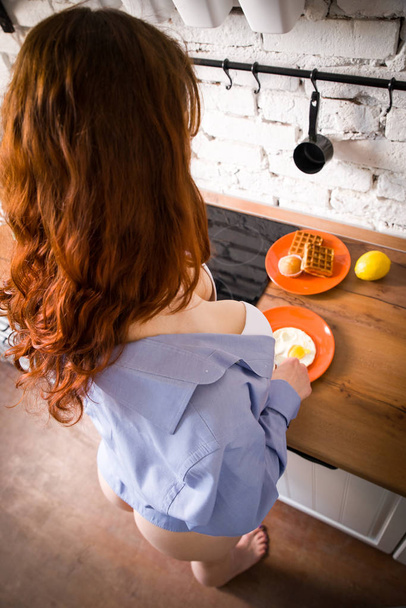 Portrait of beautiful young woman having breakfast in the kitchen. - Foto, afbeelding