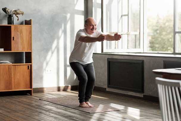 Mann praktiziert Yoga drinnen im Wohnzimmer tun Stuhlhaltung oder utkatasana - Foto, Bild