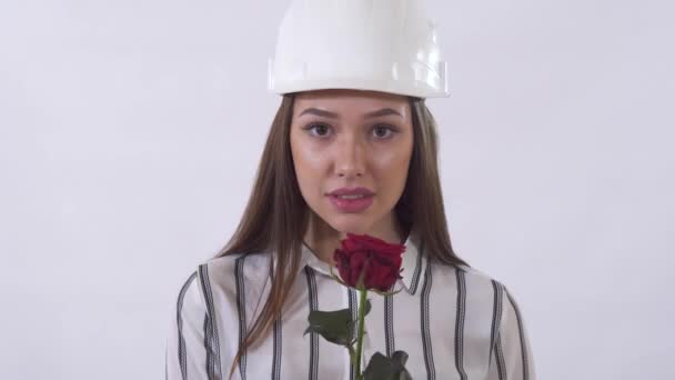 Portrait of pretty woman in helmet sniffing red rose and smiling close up. Shooting in the studio on a white background. - Imágenes, Vídeo