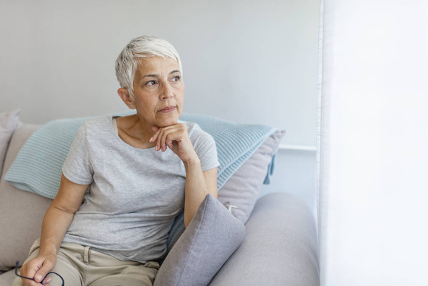 Mature grey haired woman sitting on sofa posing at home. - Photo, image