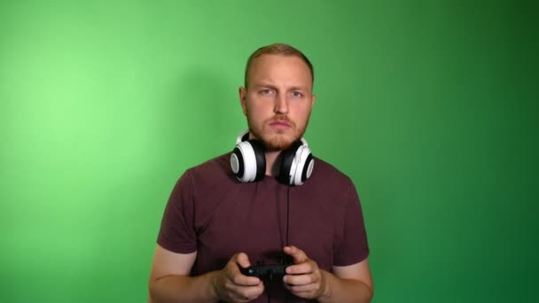 Focused man in removed headphones plays console - Imágenes, Vídeo