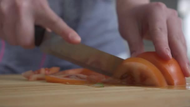 Female hand cutting tomato with a knife into thin slices on the kitchen board closeup video  - Footage, Video