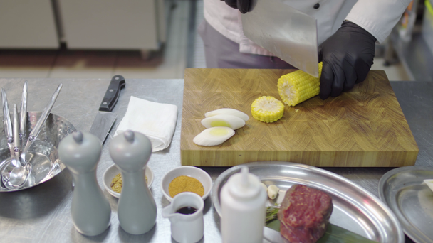 Cerca de las manos de un profesional no reconocido shuf en guantes negros están cortando maíz en trozos redondos en el tablero de la cocina en un restaurante de lujo
 - Metraje, vídeo