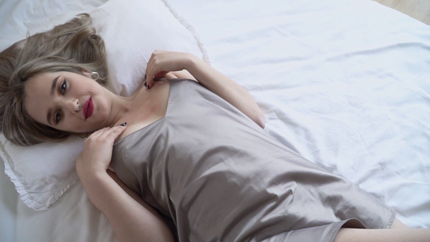 video van jonge sexy dame met heldere make-up liggend op de rug in korte nachtkleding op het bed closeup. Vrouw die hartstochtelijk haar schouders aanraakt  - Video