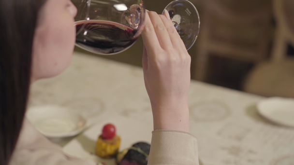 Young happy beautiful woman with long dark hair sit in the restaurant table and drinking a red wine from a big wine glass - Séquence, vidéo