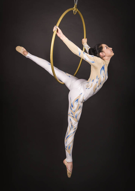 A slender,dark-haired girl - an air acrobat in a white and blue suit, performs exercises in an air ring. - Photo, image