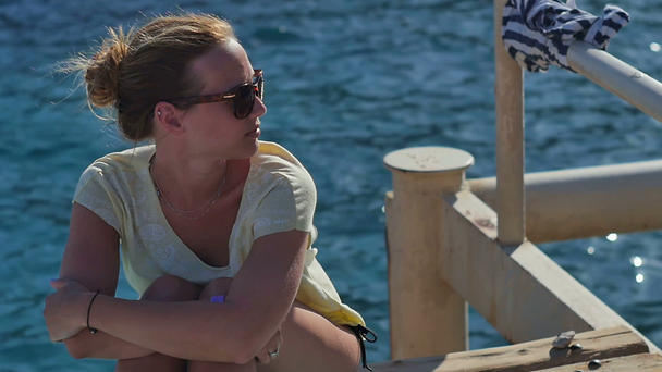 junges Mädchen mit Sonnenbrille sitzt an einem sonnigen Tag in Strandnähe - Filmmaterial, Video