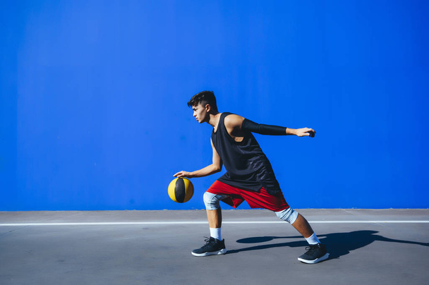 Man playing basketball in front of a blue wall - Foto, Bild