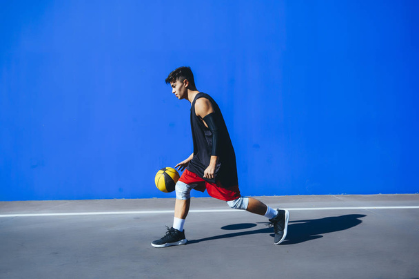 Człowiek grający w koszykówkę przed niebieską ścianą - Zdjęcie, obraz