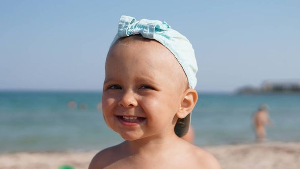 Κοντινό-up πορτρέτο του ευτυχισμένο χαμογελαστή παιδί σε μπλε καπάκι στέκεται στη θάλασσα παραλία - Φωτογραφία, εικόνα