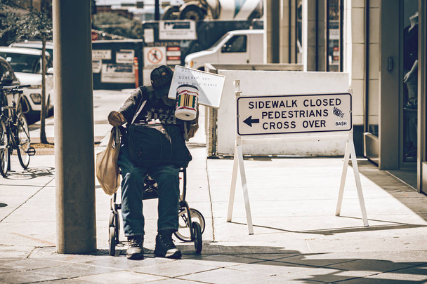 Un vagabundo está sentado en su silla de ruedas pidiendo ayuda.
. - Foto, Imagen