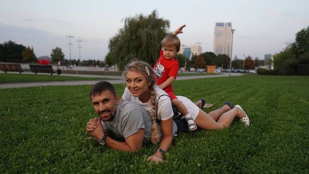 glückliche Familie - Papa, Mutter und kleiner Sohn liegen im Sommer auf dem Rasen im Park. - Foto, Bild
