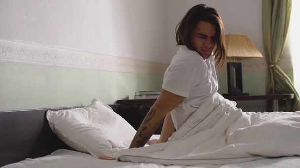 Śpiący facet w piżamie niechętnie wstaje z łóżka - Materiał filmowy, wideo