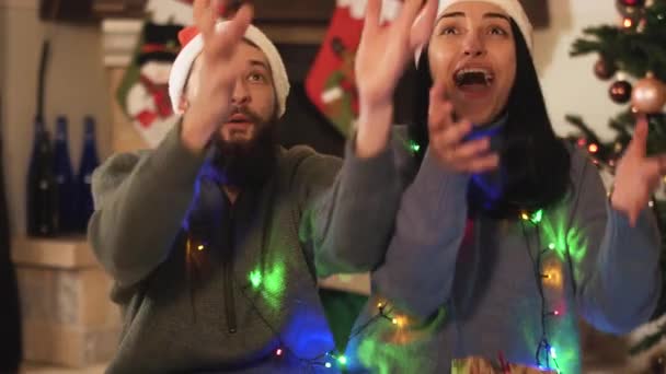 man and a woman are sitting near the New Year tree and catching gifts and laughing, video  - Imágenes, Vídeo