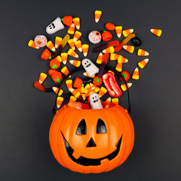 Halloween Jack o Lantern pail with spilling candy, top view on a black background - Photo, Image