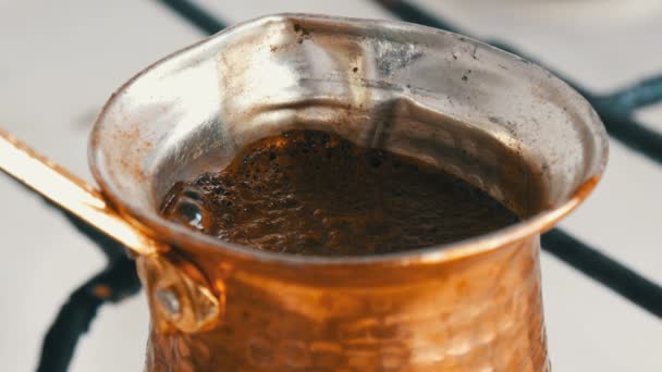 Gemalen zwarte koffie in een koper Turk wordt gebrouwen en kookt op een gasfornuis. Barista bereiden warme smakelijke drank thuis close-up - Video