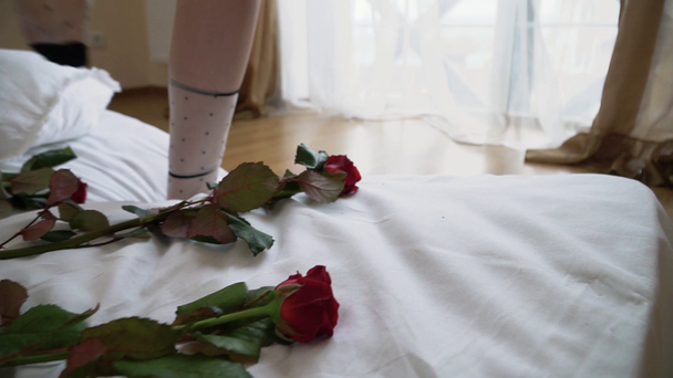 videó női láb séta matrac és gyere az ablakhoz. A vörös rózsák az előtérben fekszenek az ágyon. - Felvétel, videó