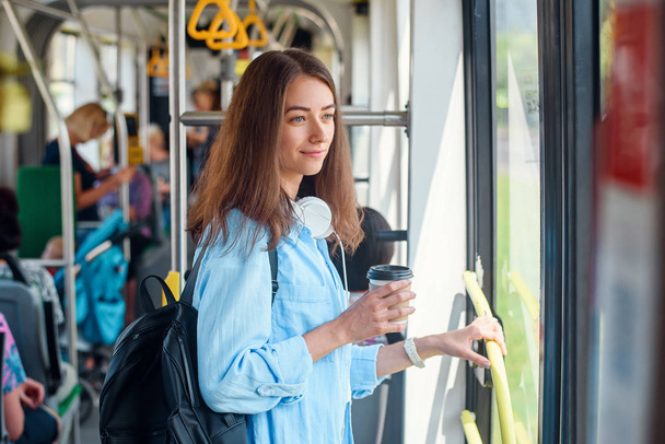 Young woman in blue shirt rides in the modern tram or bus with cup of coffee to go. - Foto, Bild