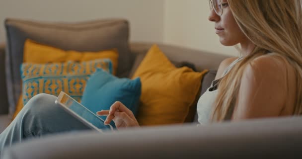 Wysokiej jakości 4K 12bit materiału Beautiful Girl za pomocą komputera typu Tablet siedzi na kanapie w domu. Kobieta surfing internetowych, sieci społecznych, patrząc coś w sklepie internetowym. Kinowy wygląd - Materiał filmowy, wideo