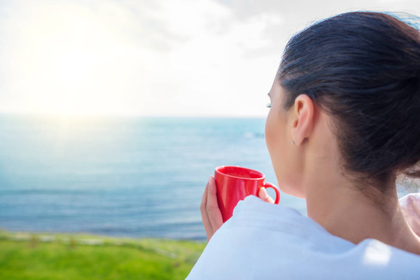 Dívka zabalená do přikrývky na balkóně ráno pije kávu nebo čaj. - Fotografie, Obrázek