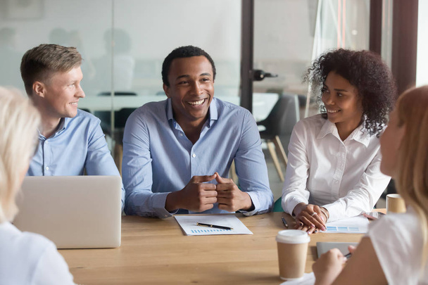 Smiling multiracial colleagues negotiate cooperating at meeting - Фото, изображение