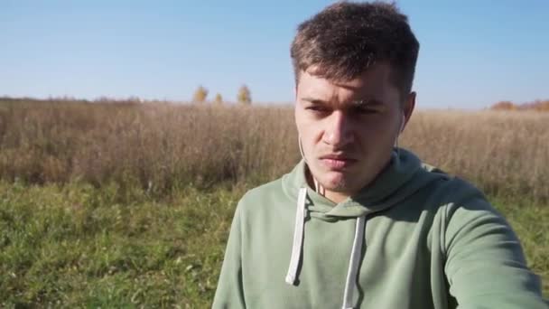 Attractive caucasian young man is walking in country side alone along fields. - Video, Çekim