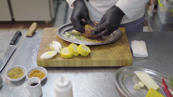 Chefs handen in zwarte latex handschoenen wrijft een stuk kalfsvlees in de metalen plaat, marineren vlees. Keukentafel met keukengerei en ingrediënten. - Video