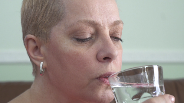 Πορτρέτο της ώριμης γυναίκας με κοντά ξανθά μαλλιά πόσιμο νερό από γυαλί, βίντεο  - Πλάνα, βίντεο