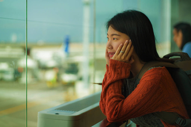 young happy and excited Asian Japanese student woman with backpack at airport departure lounge watching aircraft through glass window smiling ready for boarding - Foto, Imagen