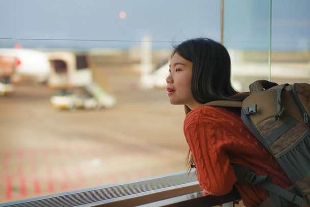 young happy and excited Asian Korean student woman with backpack at airport departure lounge watching aircraft through glass window smiling ready for boarding - Foto, Imagen