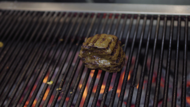 Chef bereidt smakelijk vlees op de grill, draait het met metalen tangen close-up. Rode houtskool op de bodem. Voedselbereiding in de keuken van het restaurant - Video
