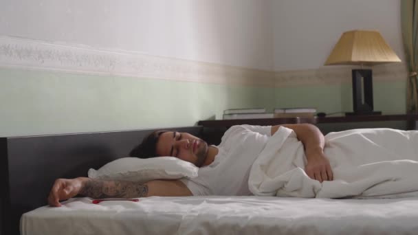 Man asleep in the wide bed wakes up looks at the phone and goes to bed and falls asleep again - Záběry, video