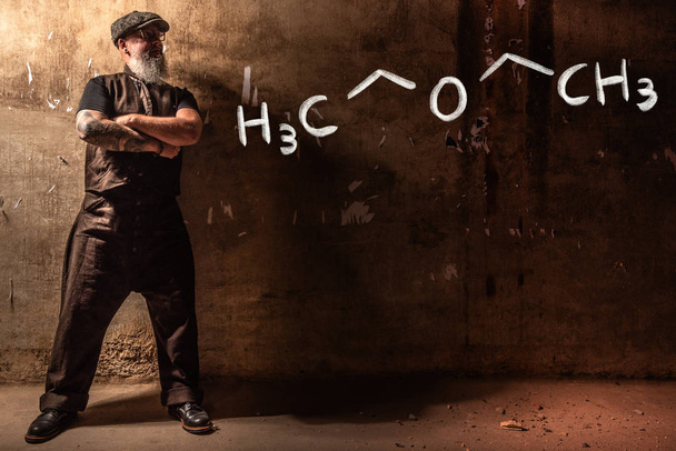 Parrakas vanha mies esittelee käsin piirrettyä kemiallista kaavaa Dietyylieetteristä
 - Valokuva, kuva
