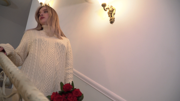 vídeo de mujer con ramo de rosas bajando escaleras. Mujer joven en suéter corto de invierno y medias está dentro de la casa grande
 - Metraje, vídeo