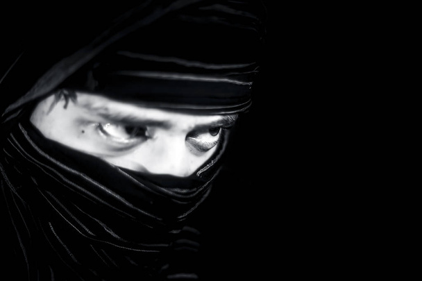 Striking portrait of male teenager isolated on black with piercing expressive eyes along with a cloth covering face except eyes.Expressing boldness and Courage. - Photo, image