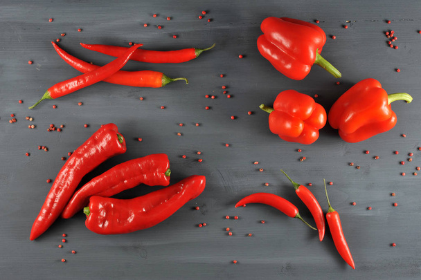 Sweet pepper, Ramiro, hot cayenne chili pepper on a dark surface. All the pepper is red. Around are scattered peas of pink pepper. Close-up. View from above. - 写真・画像