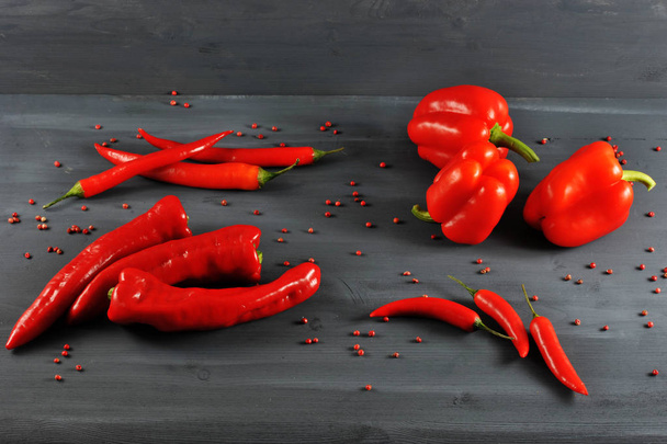Sweet pepper,  Ramiro, hot cayenne chili pepper on a dark surface. All the pepper is red. Around are scattered peas of pink pepper. Close-up. - 写真・画像