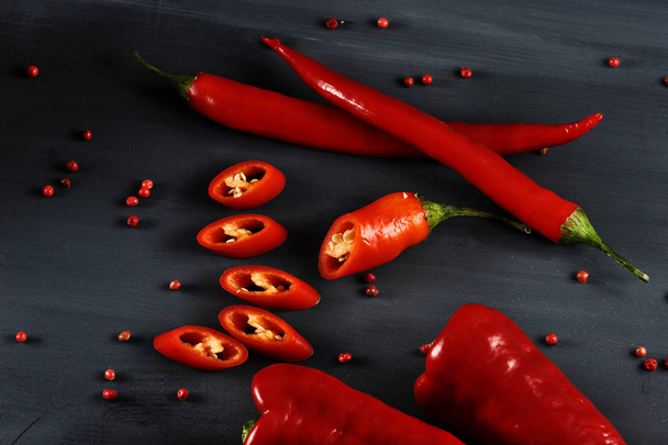 Spicy cayenne pepper on a dark background. In the frame is also a variety of sweet pepper Ramiro. One hot chili pepper is cut into mugs. Pears of pink pepper are scattered on the surface. Close-up. - Foto, imagen