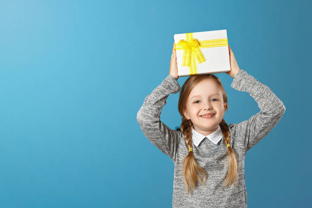 Happy little girl holding box with gift above head. Portrait of a child on a blue background. Copy space. - Photo, Image