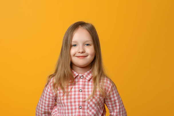 Closeup portrait of a funny little blond girl on yellow background. A child in a pink shirt is looking into the camera. - Fotoğraf, Görsel
