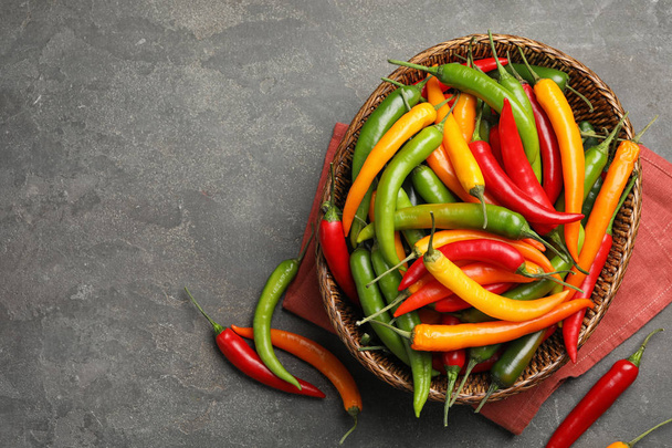 Wicker bowl with different chili peppers on grey table, flat lay. Space for text - Fotoğraf, Görsel