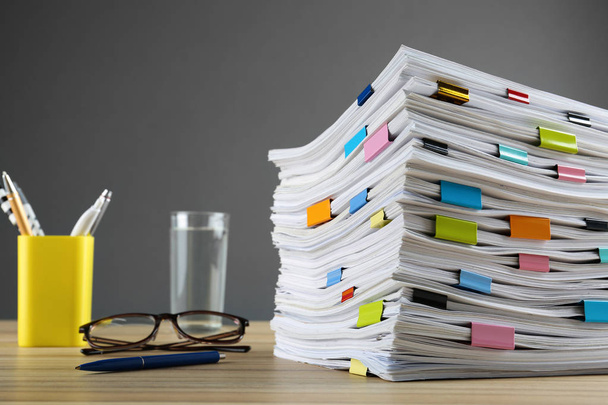 Stack of documents with binder clips and glasses on wooden table against grey background - Foto, Imagen