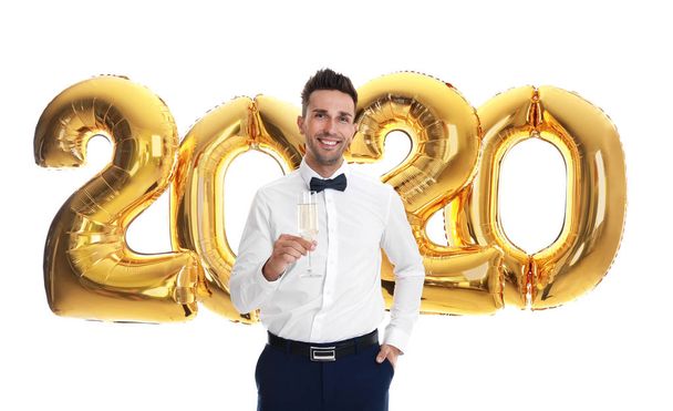 Happy young man with glass of champagne near golden 2020 balloons on white background. New Year celebration - Foto, afbeelding