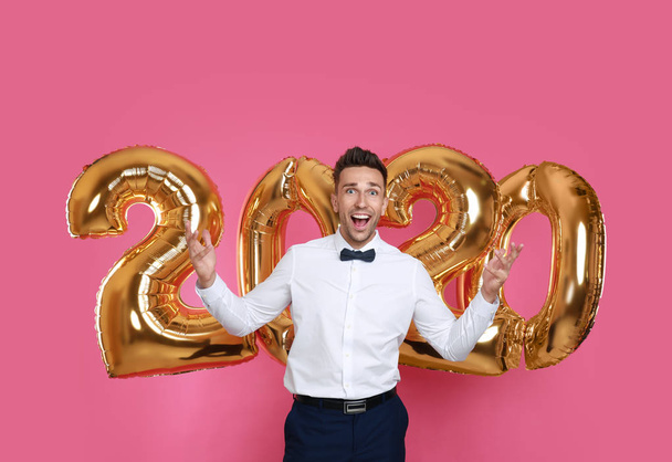Happy young man near golden 2020 balloons on pink background. New Year celebration - Foto, imagen