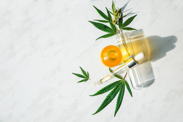 Glasflasche mit Cannabisöl und Reagenzglas mit Hanfblättern auf Marmorgrund. Kopierraum. - Foto, Bild