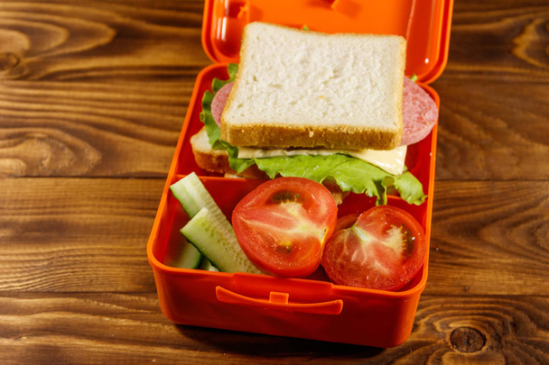 Школьная коробка с бутербродом и свежими овощами на деревянном столе
 - Фото, изображение