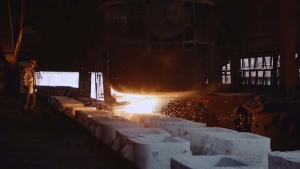 Fundición de hierro. Un trabajador siderúrgico con ropa protectora supervisa la fundición de acero en moldes
. - Imágenes, Vídeo