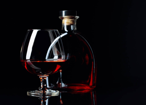 Glas und Flasche Brandy auf schwarzem, reflektierendem Hintergrund.  - Foto, Bild