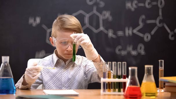 Little chemist in protective glasses checking reaction in tube with green liquid - Foto, Bild